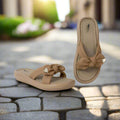 Pair of beige sandals with bow design on a pink background
